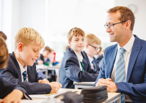 student writing as a teacher looks on