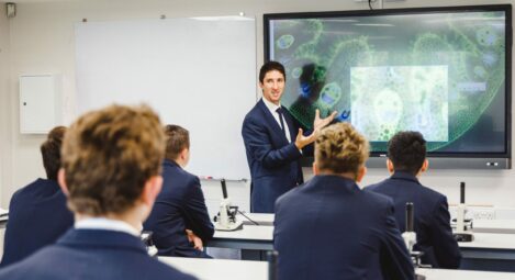 A teacher speaking to students in a Biology class. Students have microscopes on their desks