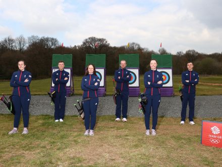3 men and 3 women smiling behind archery targets ahead of the competition