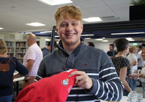 students holding his school jumper and smiling
