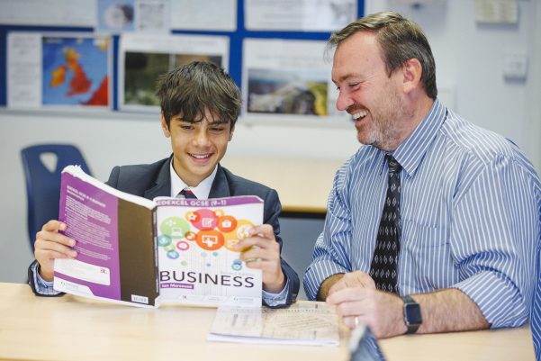 student holding a business text book and reading to teacher