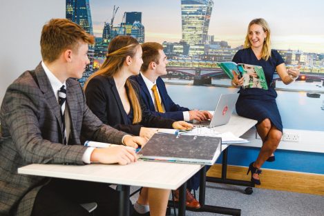 teacher leaning on desk as she teaches pupils