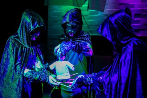 three boys stood in a circle wearing black cloaks