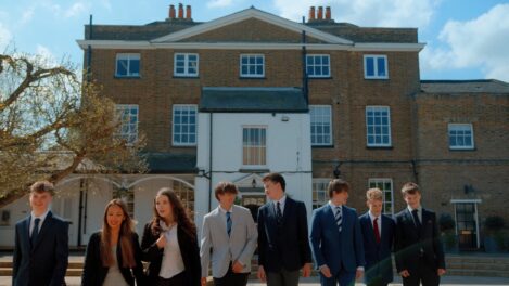 Group of smiling students in suits walking outside a brick building on a sunny day.