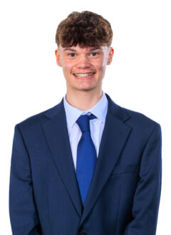 Smiling young man in a navy suit and blue tie against a white background, office portrait style.