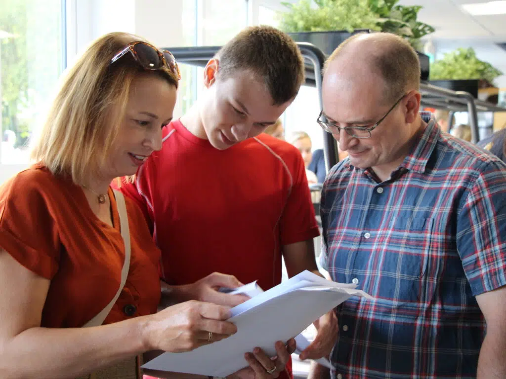 Three adults closely examining papers together in a bright indoor setting.