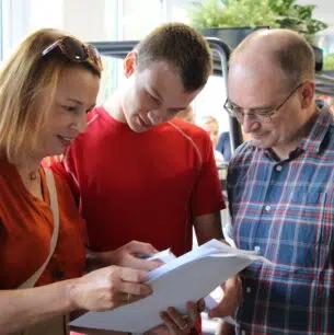 Three adults closely examining papers together in a bright indoor setting.
