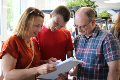 Three adults closely examining papers together in a bright indoor setting.