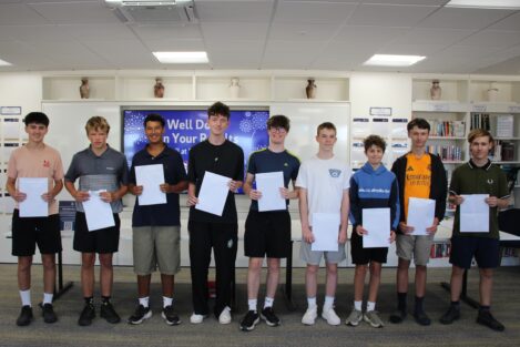 Ten students stand in a school library, each holding a certificate.